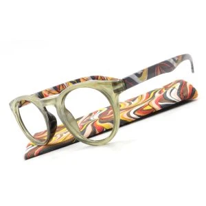 Augenstolz Fertiglesebrille Blixt Gold – runde Lesebrille mit transparent-goldenem Rahmen, schräg auf dem Etui mit orange-braun-gelbem Wellenmuster liegend